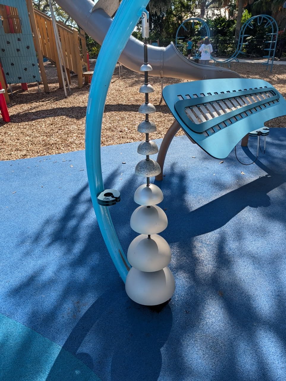 Outdoor sensory playground musical chimes with silver bell bowls on a blue safety surface.